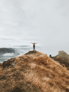 person standing on top of a hill arms stretched out to the side
